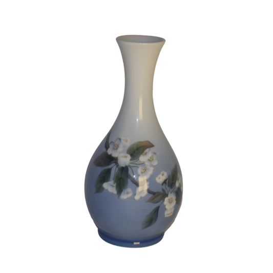 En elegant Royal Copenhagen vase med en lysblå krop og hvide kirsebærblomster grene, der strækker sig op mod den hvide hals.